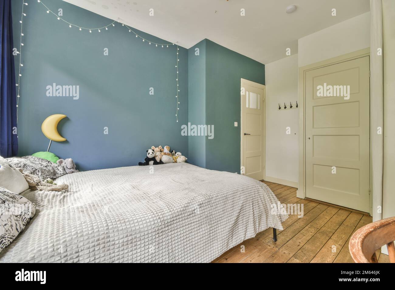 Ein Schlafzimmer mit blauen Wänden und weißer Bettwäsche, Holzfußboden und Lichterketten, die von der Decke hängen Stockfoto