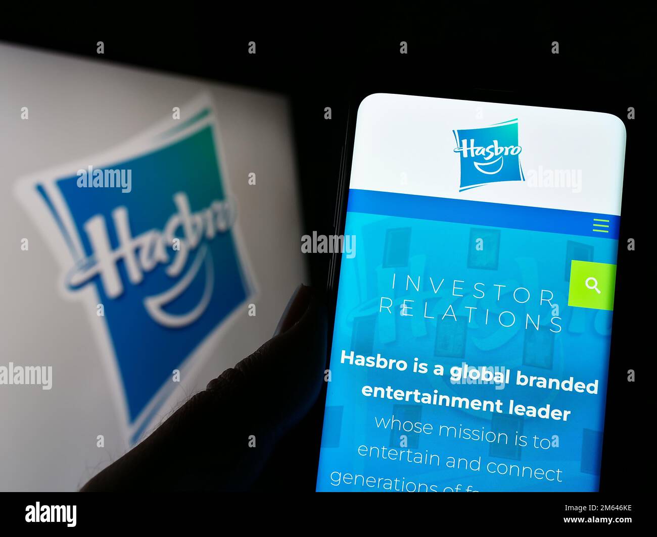 Person, die ein Mobiltelefon mit einer Website des US-amerikanischen Spielzeugunternehmens Hasbro Inc. Auf dem Bildschirm mit Logo hält. Konzentrieren Sie sich auf die Mitte des Telefondisplays. Stockfoto