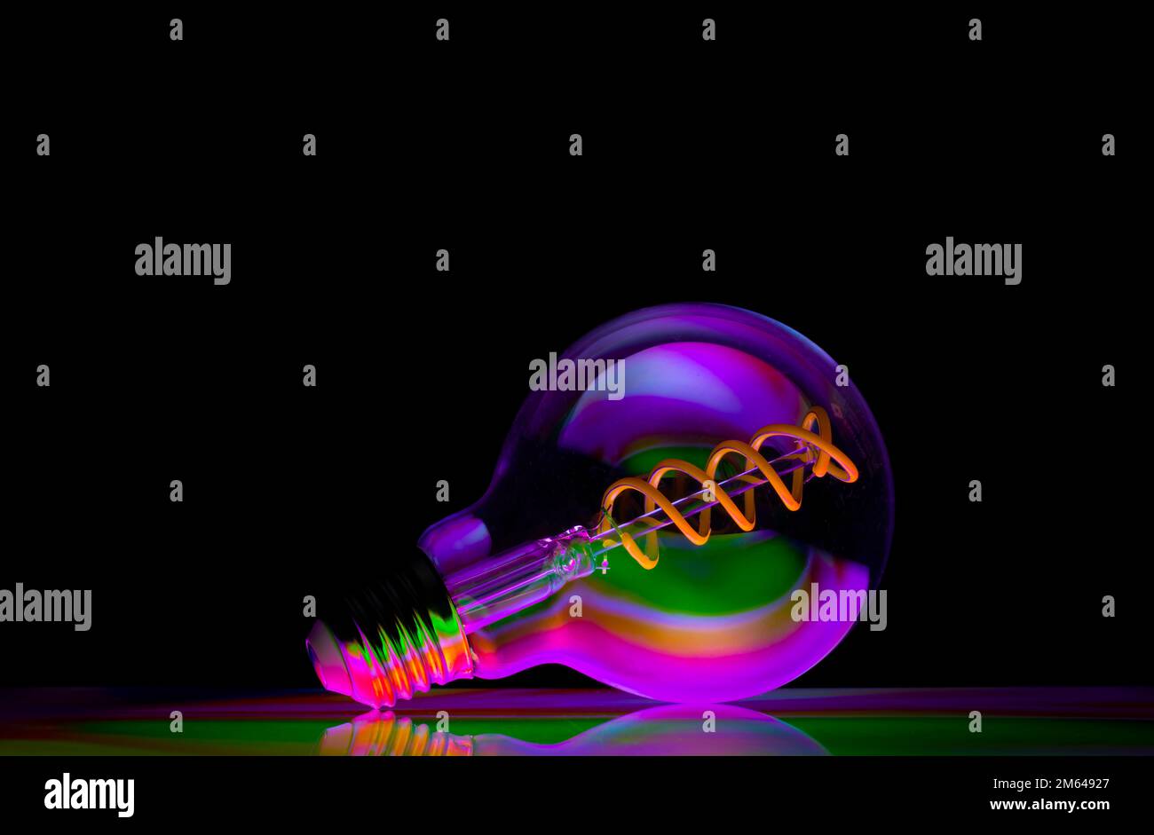 Bunte Muster spiegeln sich in einer runden Glühbirne aus klarem Glas wider, die vor schwarzem Hintergrund fotografiert wird Stockfoto