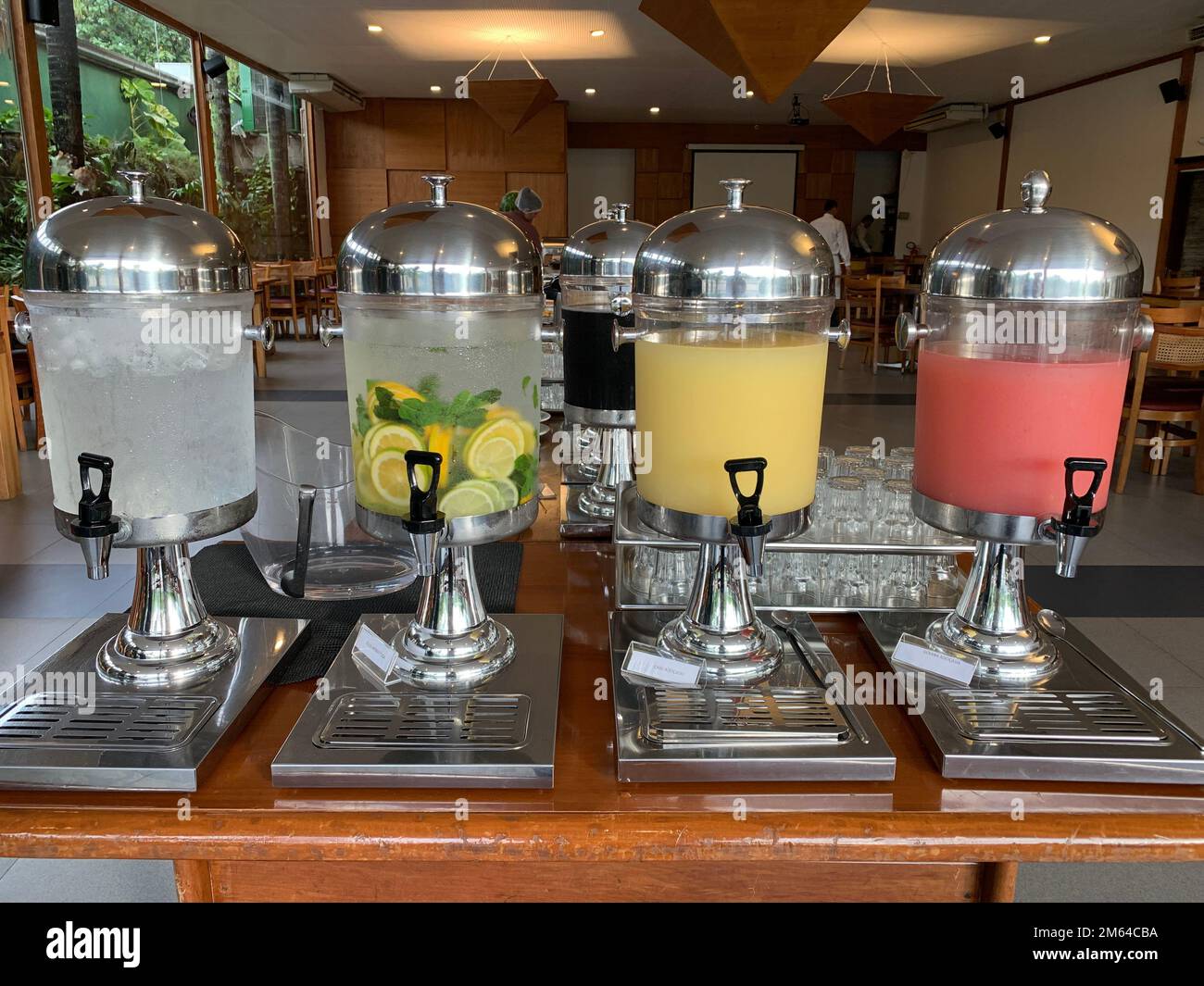 Vier transparente Getränkeautomaten mit Wasserhahn, gefüllt mit Wasser, Guavasaft, Cashewsaft und aromatischem Wasser auf einem Buffet-Tisch Stockfoto