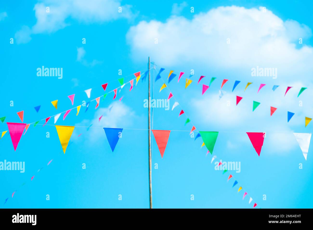 Bunte kleine Flaggen am Himmel. Winkende kleine bunte Flaggen, die am Seil hängen, um Urlaub vor blauem Himmel zu machen. Stockfoto