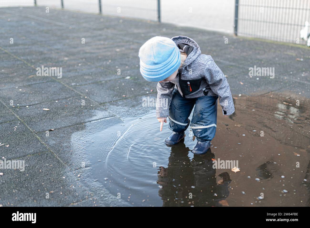 Zwei Jahre alter Junge in Regenhosen und Gummistiefeln, der nach einem Regenschauer in einer Wasserpfütze spielte Stockfoto