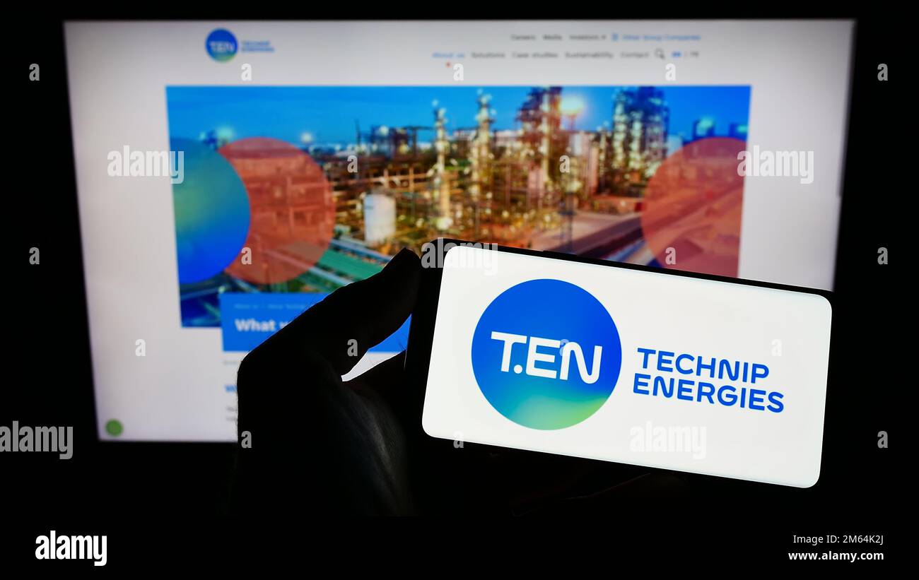 Person, die ein Mobiltelefon mit dem Logo des französischen Ingenieurunternehmens Technip Energies NV auf dem Bildschirm vor der Webseite hält. Konzentrieren Sie sich auf das Display des Telefons. Stockfoto