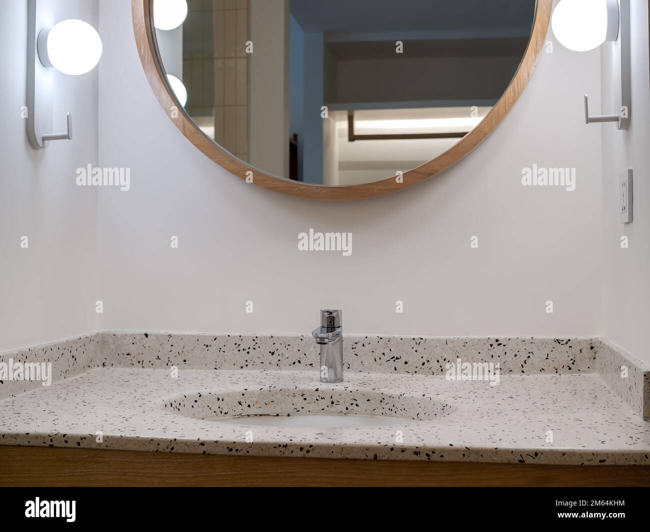 Armatur oder Wasserhahn aus rostfreiem Chrom-Silber in runder Form von Terrazzo-Fliesen Waschbeckendekoration mit rundem Spiegel und Lampen auf weißem Wandschrank Stockfoto