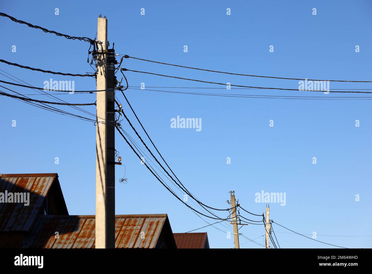 Powerline-Pfosten mit elektrischen Drähten und Kondensatoren über alten Dächern auf blauem Himmelshintergrund. Stromleitung, Stromversorgung im Dorf Stockfoto