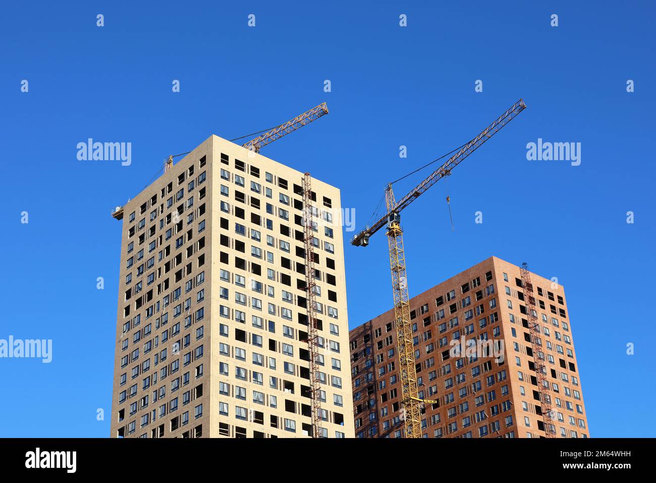 Turmkräne und zwei unfertige Gebäude vor blauem Himmel. Wohnungsbau, Wohnblocks in der Stadt Stockfoto