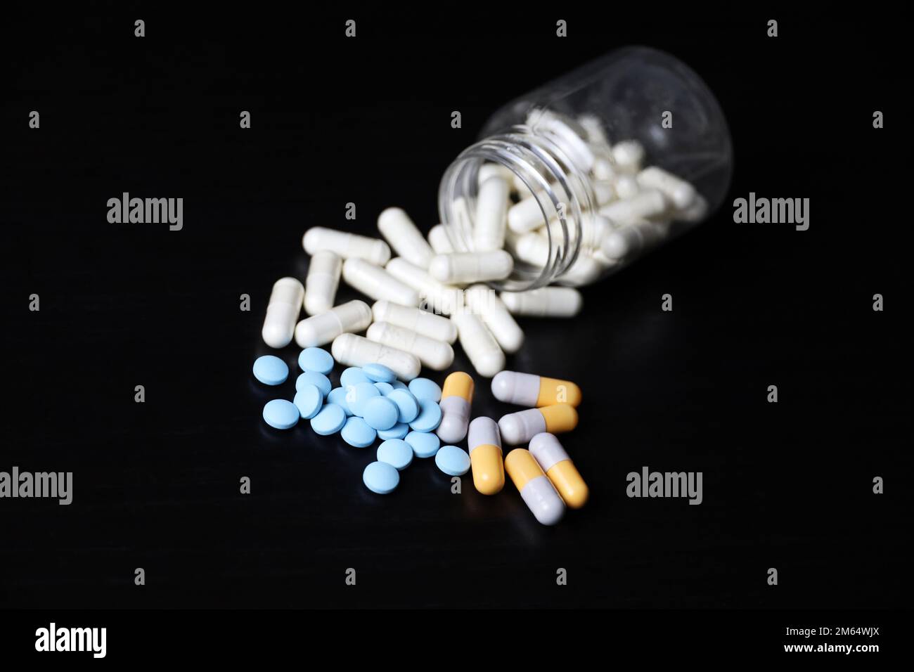 Verschiedene Pillen auf einem schwarzen Holztisch, Variation der Medikamente in Kapseln, die aus einer Flasche verstreut sind. Hintergrund für Pharmazie, Antibiotika, Vitamine Stockfoto