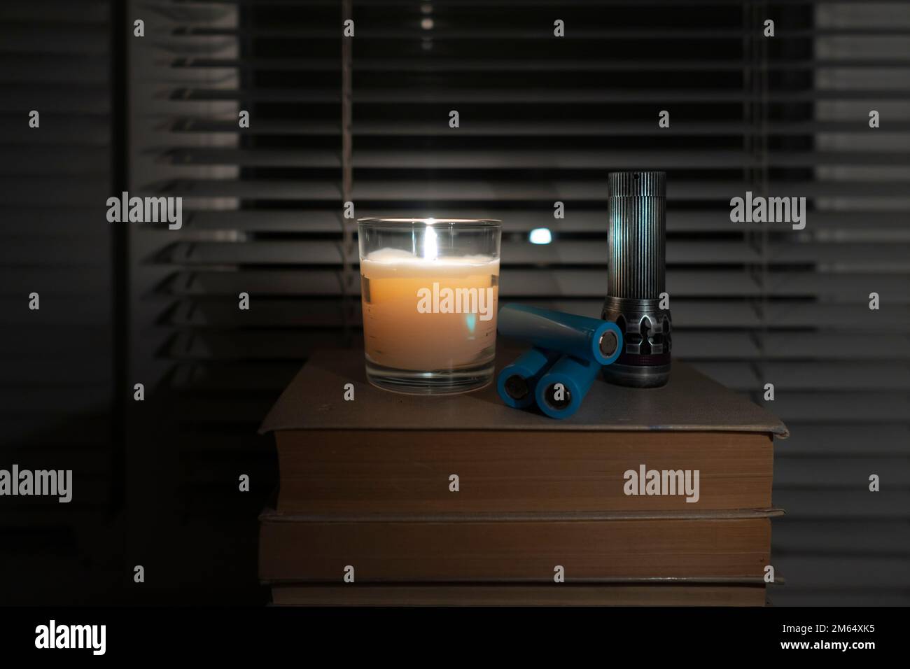 Eine Taschenlampe und wiederaufladbare Batterien liegen in einem dunklen, leeren Raum neben dem Fenster bei Kerzenlicht (Nahaufnahme). Stromausfall. Energiekrise Stockfoto