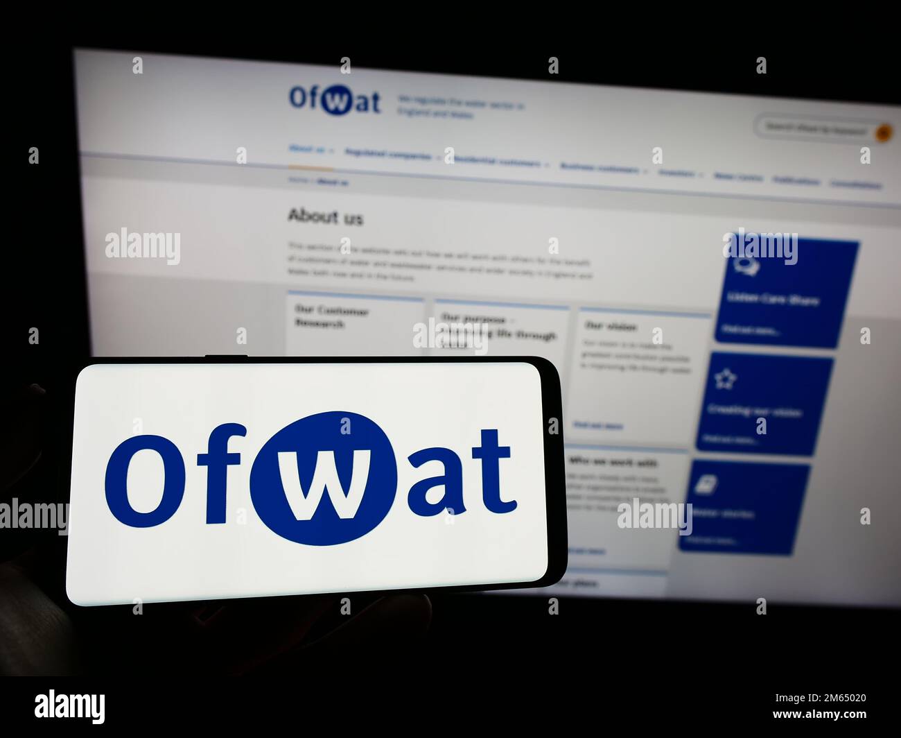 Person, die ein Mobiltelefon mit dem Logo der Wasserdienstaufsichtsbehörde (Water Services Regulation Authority, Ofwat) auf dem Bildschirm vor der Webseite hält. Konzentrieren Sie sich auf das Display des Telefons. Stockfoto