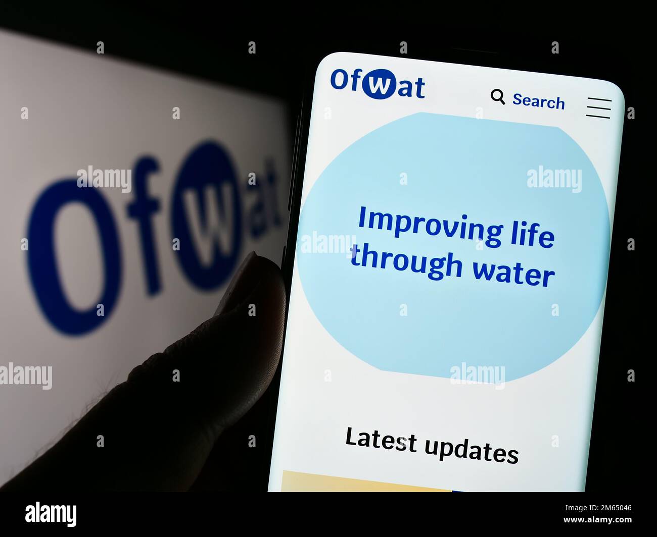 Person, die ein Mobiltelefon mit einer Website der Wasserdienstaufsichtsbehörde (Water Services Regulation Authority, Ofwat) auf dem Bildschirm vor dem Logo hält. Konzentrieren Sie sich auf die Mitte des Telefondisplays. Stockfoto