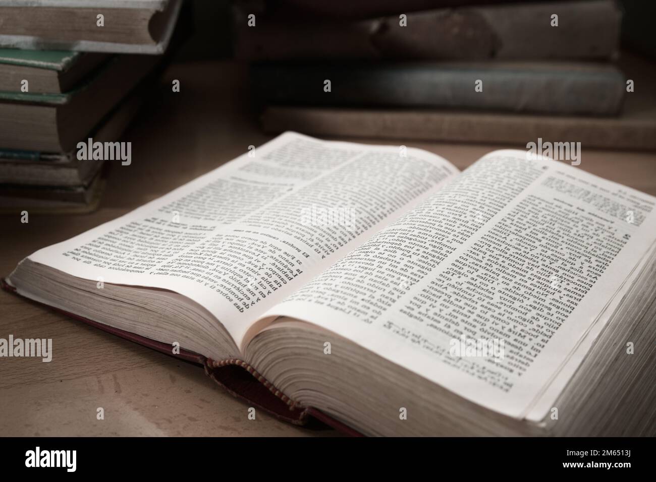 Bild eines alten Buches, das durch eine zufällige Seite auf einem Tisch geöffnet wird, mit vielen anderen alten Büchern in verschiedenen Farben Stockfoto