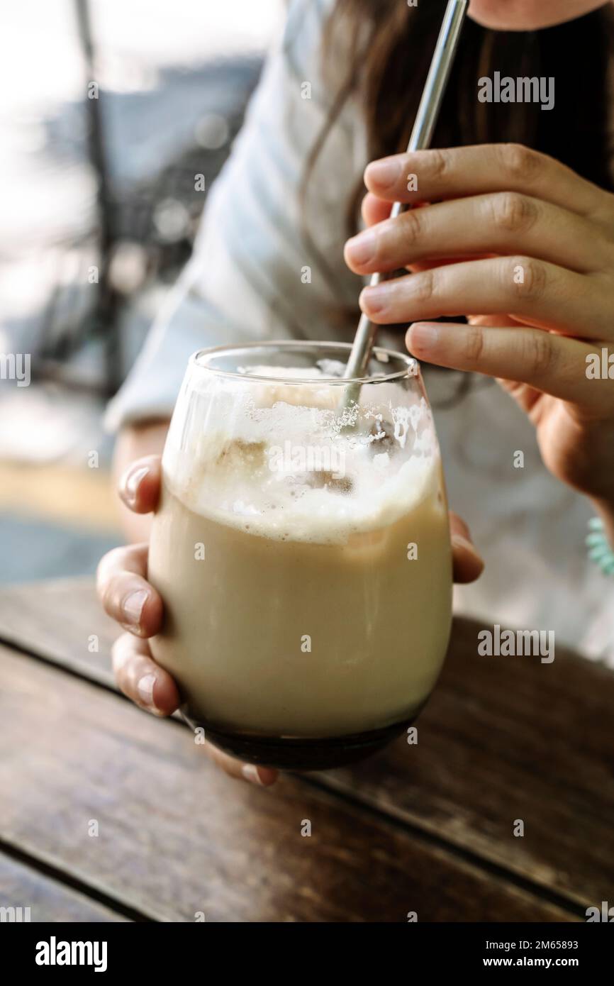 Eiskaffee in der Hand. Ein Glas kalten Kaffeegetränks mit Milch in der Hand eines Mädchens in einem Sommerkaffee auf der Straße. Drink, Lifestyle, Stadtkonzept. Hochwertiges Foto Stockfoto