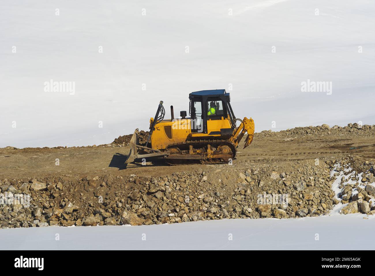 Unerkannter Arbeiter, der im Winter auf Straßenbaustellen in den Zlatibor Hills Schwerlastmaschinen mit industriellem Bulldozer fährt Stockfoto