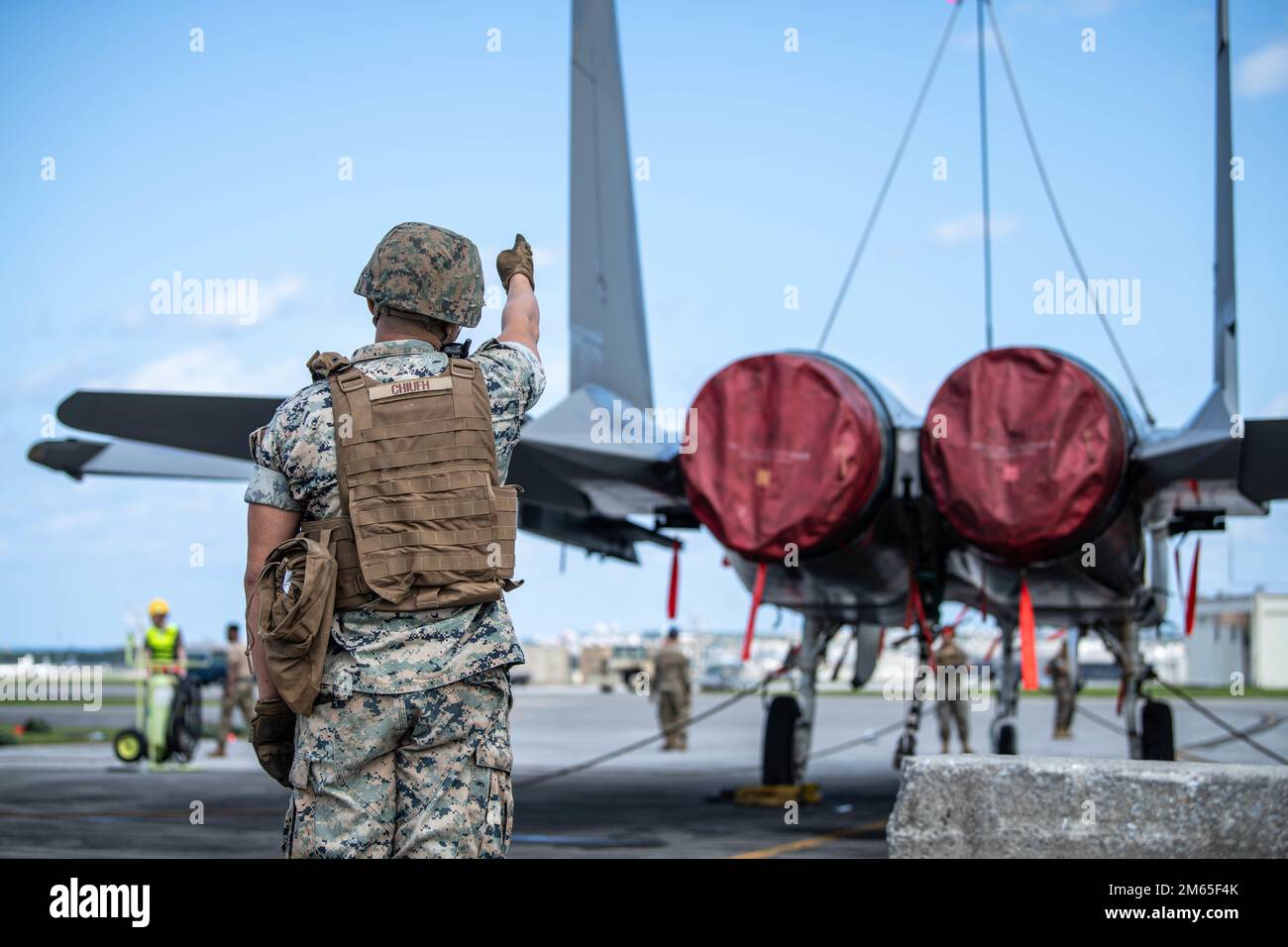 EIN US-AMERIKANISCHER Ein Marine, das der Marineflügelstaffel 172 zugewiesen wurde, überprüft die Ausrichtung eines F-15 Eagle mit einem Geländekran, bekannt als MAC-50, am Kadena Air Base, Japan, 4. April 2022. Diese gemeinsame Schulung wurde durchgeführt, um die Crash Recovery-Fähigkeiten für MWSS-172 und 18. EMS zu testen. Der MAC-50 würde zum Anheben eines unbeweglichen Flugzeugs verwendet, damit ein Lkw unter dem Flugzeug fahren und das Flugzeug für den Transport vorbereiten könnte. Stockfoto
