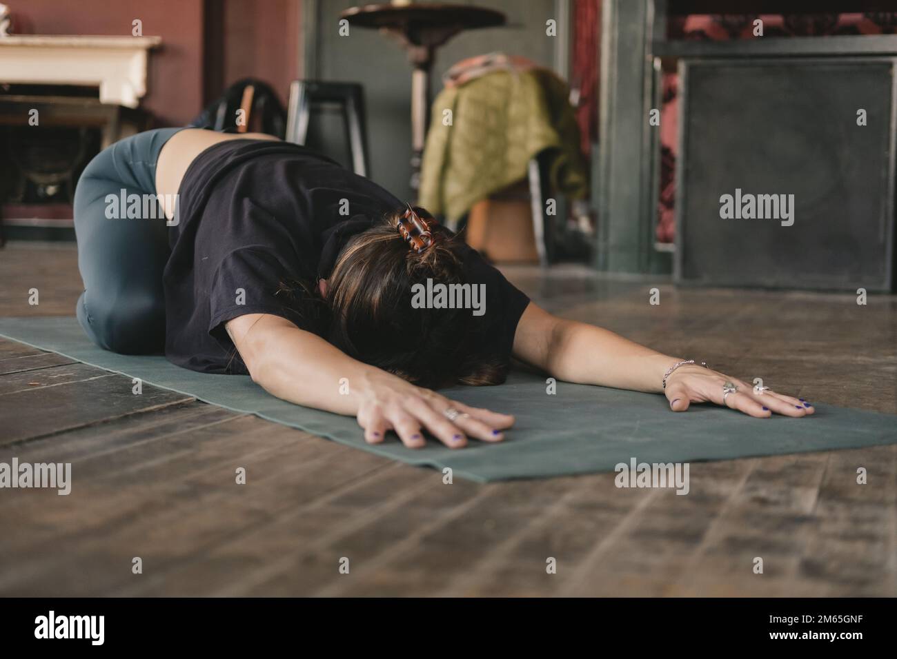 Ganzkörperfoto von weiblichem Yoga, das sich in der Kinderhaltung ruht (Balasana), mit ausgestreckten Armen während ihres Vinyasa-Flow-Yoga-Trainings allein in Sportbekleidung Stockfoto