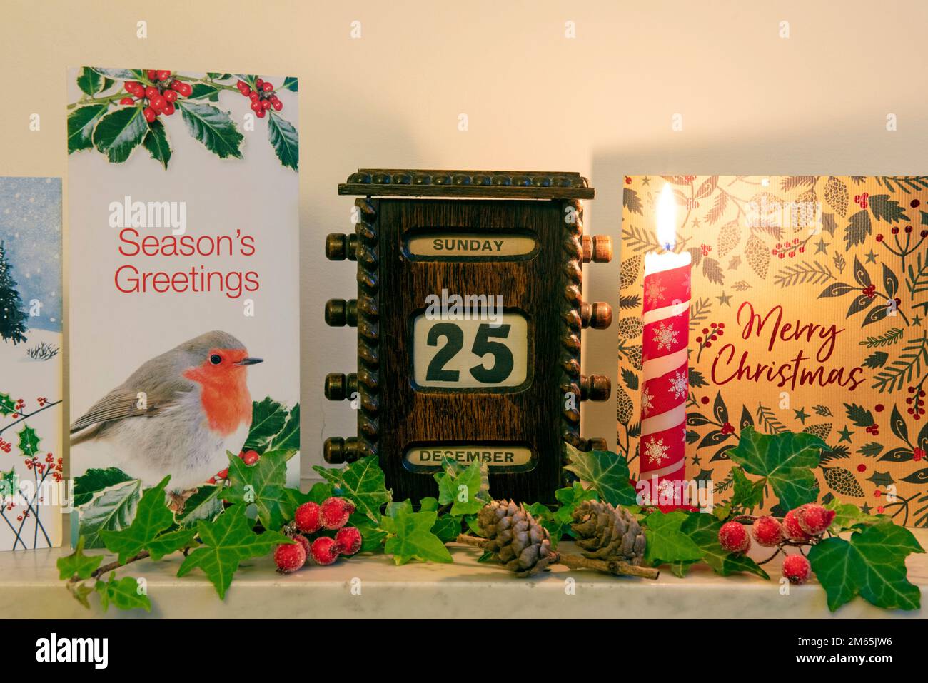 Weihnachtskarten mit beleuchteter Kerze und altem Kalender aus Holz, der den 25. Dezember auf dem Kaminsims zeigt Stockfoto