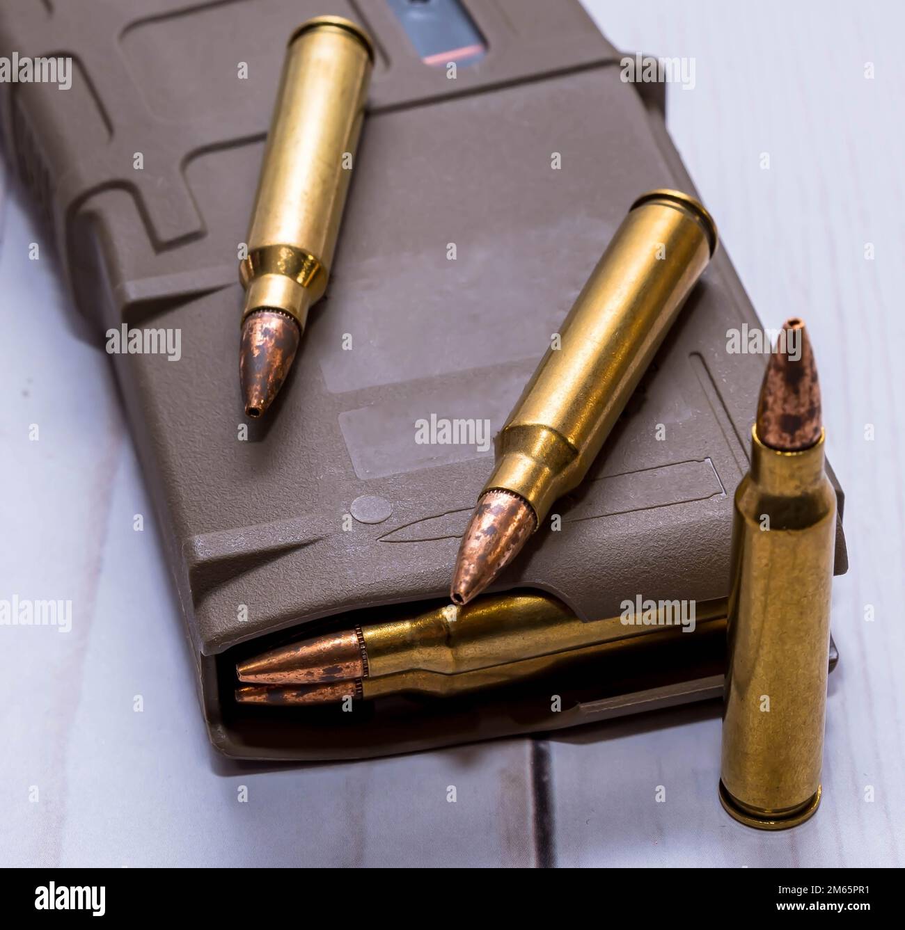 Ein AR15-Gewehrmagazin mit 223-Kaliber-Kugeln und drei zusätzlichen Kugeln daneben auf weißem Holzhintergrund Stockfoto