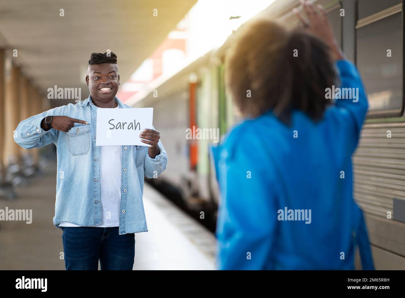 Black Man Trifft Freundin Mit Persönlicher Namenskarte Am Bahnhof Nach Der Ankunft, Stockfoto