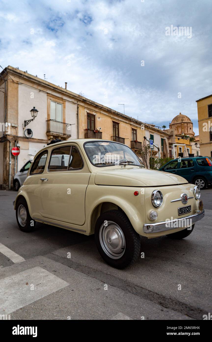 Ein vertikales Bild eines cremefarbenen Fiat 500 Autos, das in einer ruhigen Straße einer Stadt geparkt ist Stockfoto