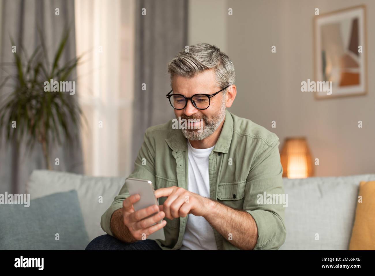 Glücklicher älterer, weißer Mann mit Brille, der auf dem Smartphone tippt, nutzt eine neue App für die Kommunikation Stockfoto