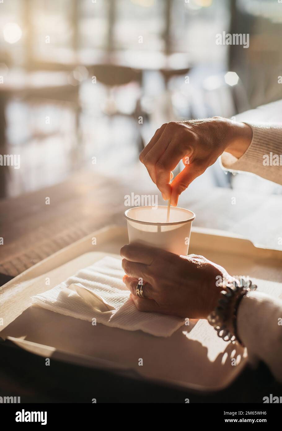 Nahaufnahme einiger Hände mit einem Kaffee. Die Person rührt den Kaffee mit einem Löffel. Das Licht ist natürlich und warm. Entspannendes Konzept bei einem Kaffee Stockfoto