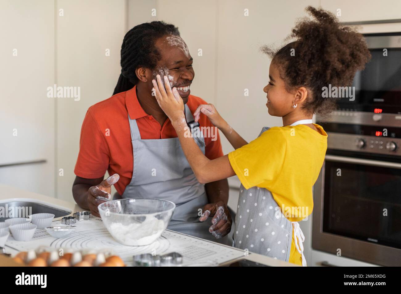 Fröhliches Schwarzes Mädchen Spielt Mit Dad In Kitchen, Während Sie Zusammen Backen Stockfoto