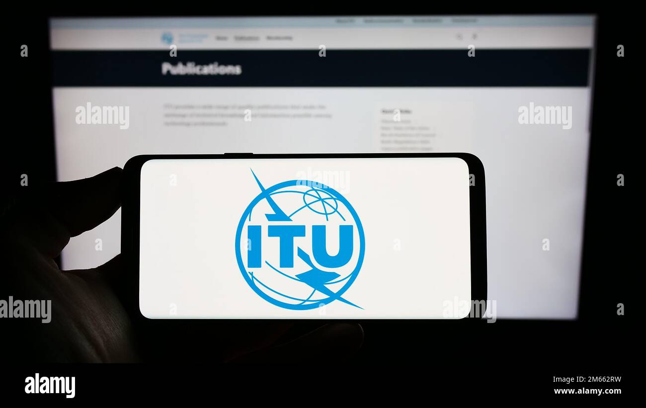 Person, die ein Mobiltelefon mit dem Logo der Internationalen Fernmeldeunion (ITU) auf dem Bildschirm vor der Webseite hält. Konzentrieren Sie sich auf das Display des Telefons. Stockfoto