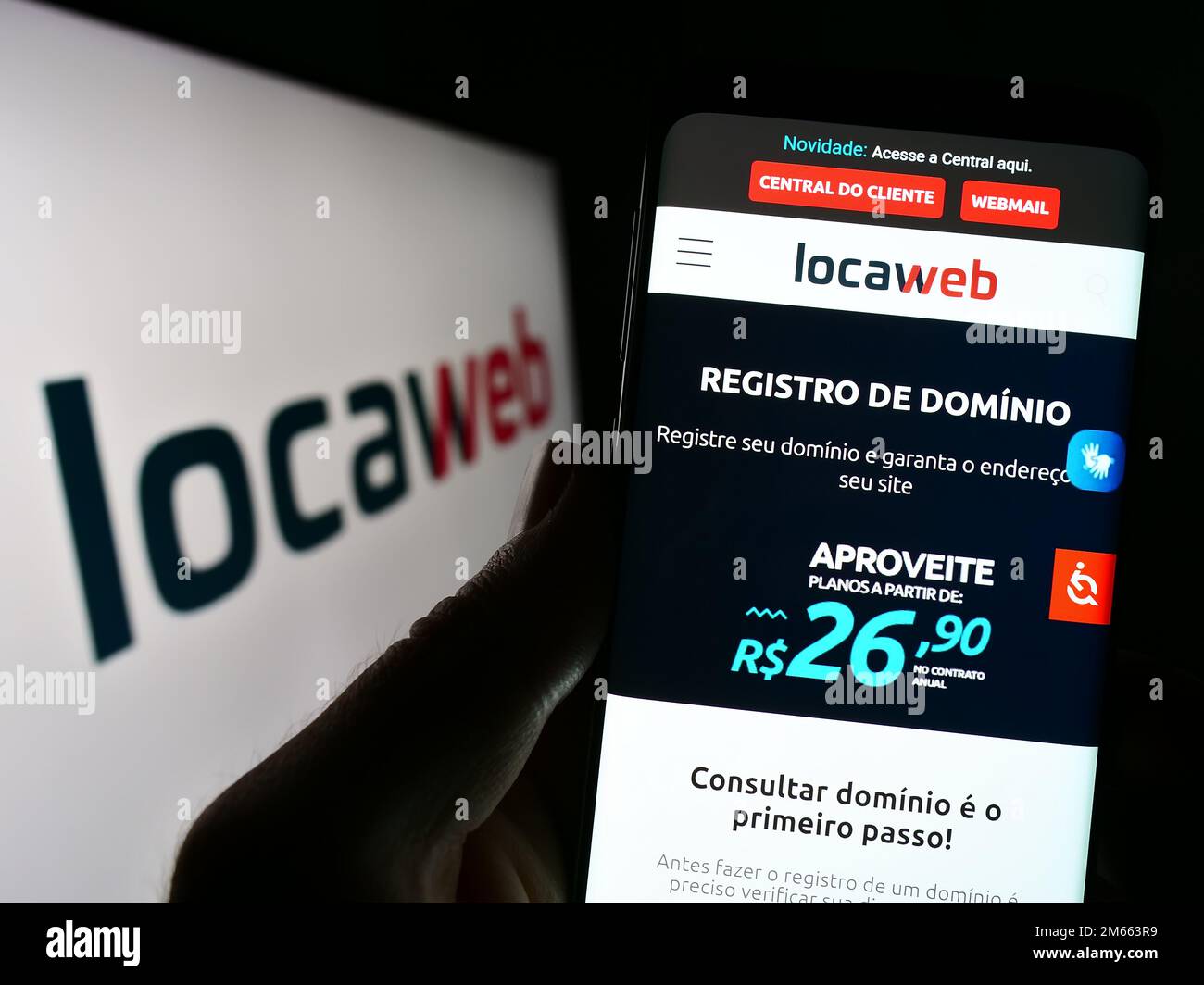 Person, die ein Mobiltelefon mit der Website des brasilianischen Webhostingunternehmens Locaweb auf dem Bildschirm vor dem Logo hält. Konzentrieren Sie sich auf die Mitte des Telefondisplays. Stockfoto