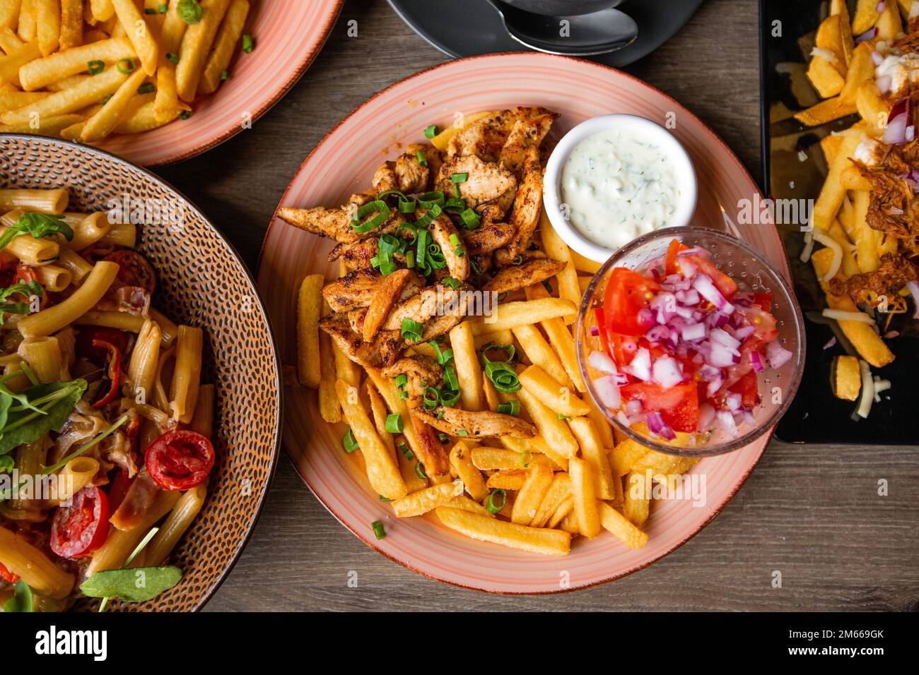 Nahaufnahme von frischem leckerem Junkfood aus pommes frites, Kartoffel mit Knoblauchsoße, Gemüsesalat, Tomatenpasta, Fleischplatte Stockfoto