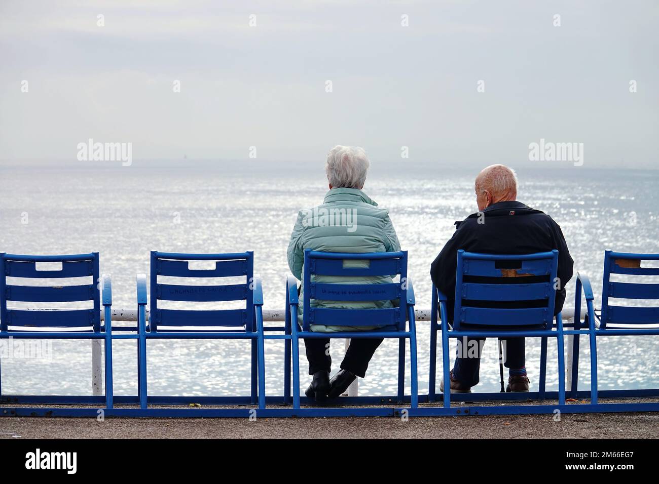 Menschen, die am Meer auf den berühmten blauen Stühlen in Nizza auf der Promenade des Anglais sitzen. Nizza, Frankreich - 2022. Dezember Stockfoto