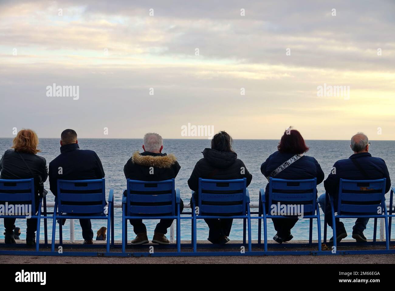 Menschen, die am Meer auf den berühmten blauen Stühlen in Nizza auf der Promenade des Anglais sitzen. Nizza, Frankreich - 2022. Dezember Stockfoto