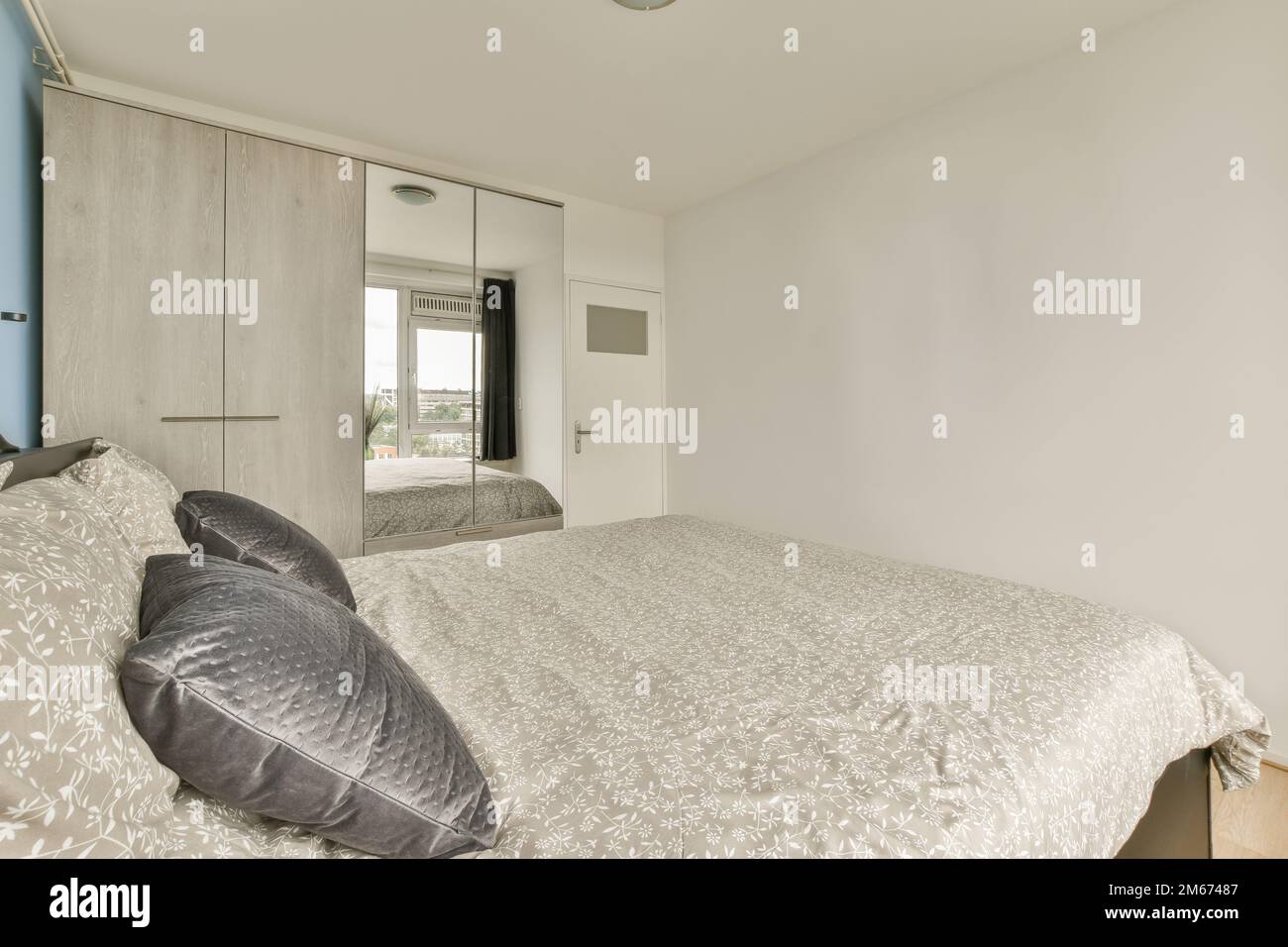 Ein Schlafzimmer mit einem Bett und Spiegel an der Wand neben den Schränken des anderen Zimmers Stockfoto