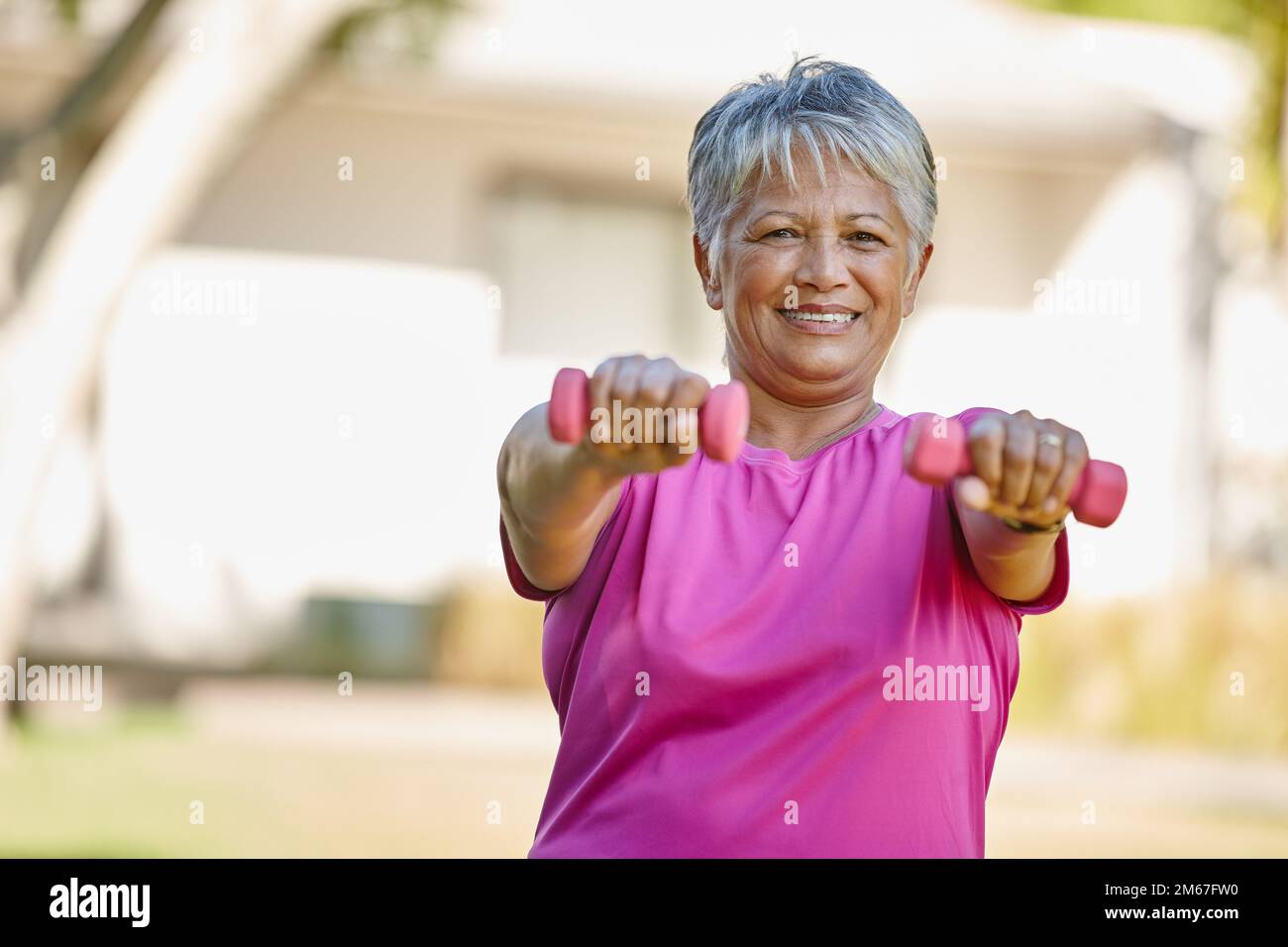 Hier wird man nicht alt. Porträt einer erwachsenen Frau, die draußen Kurzhanteln hebt. Stockfoto