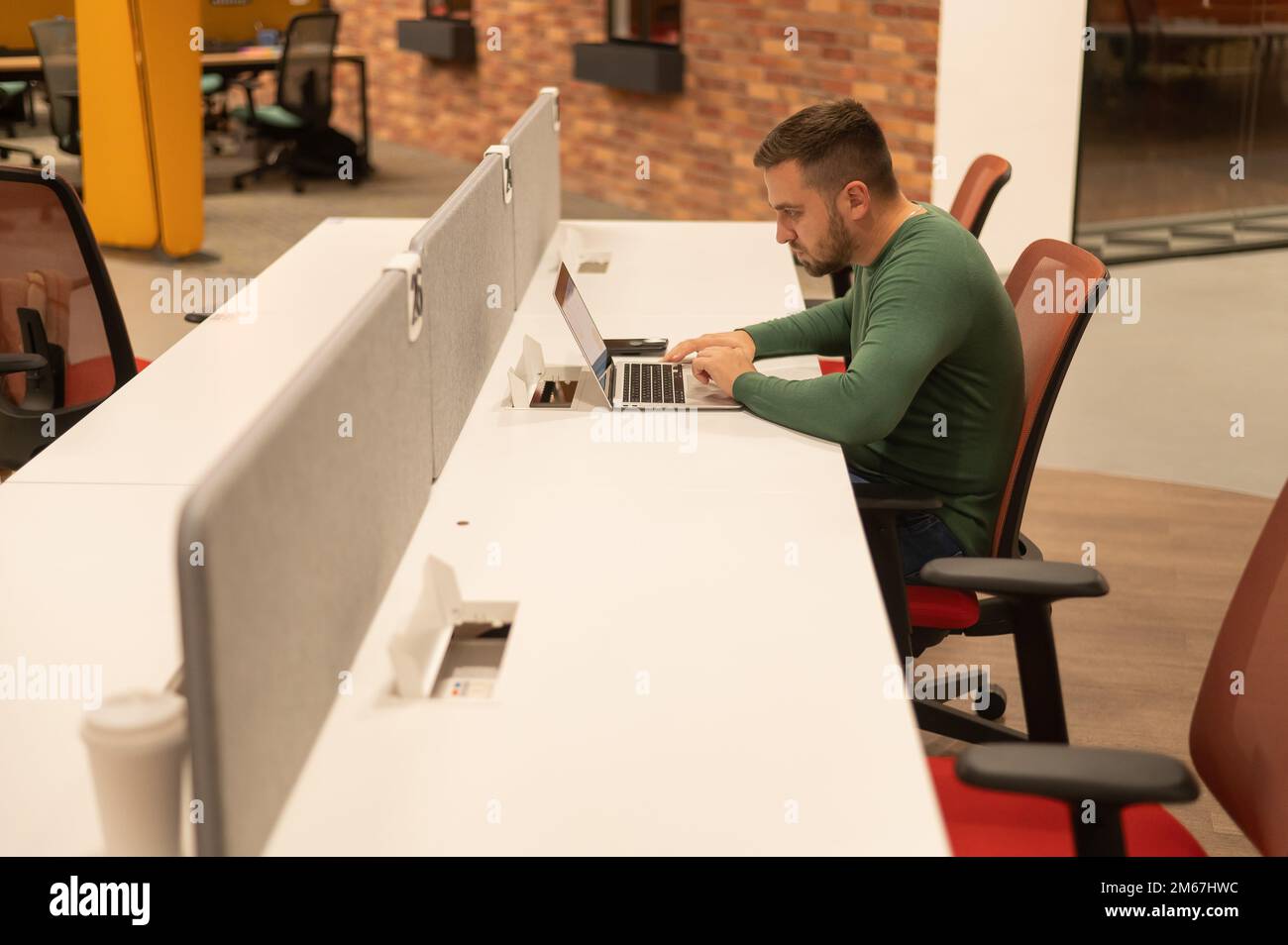 Weißer bärtiger Mann, der an einem Laptop in einem modernen Gemeinschaftsraum arbeitet. Stockfoto