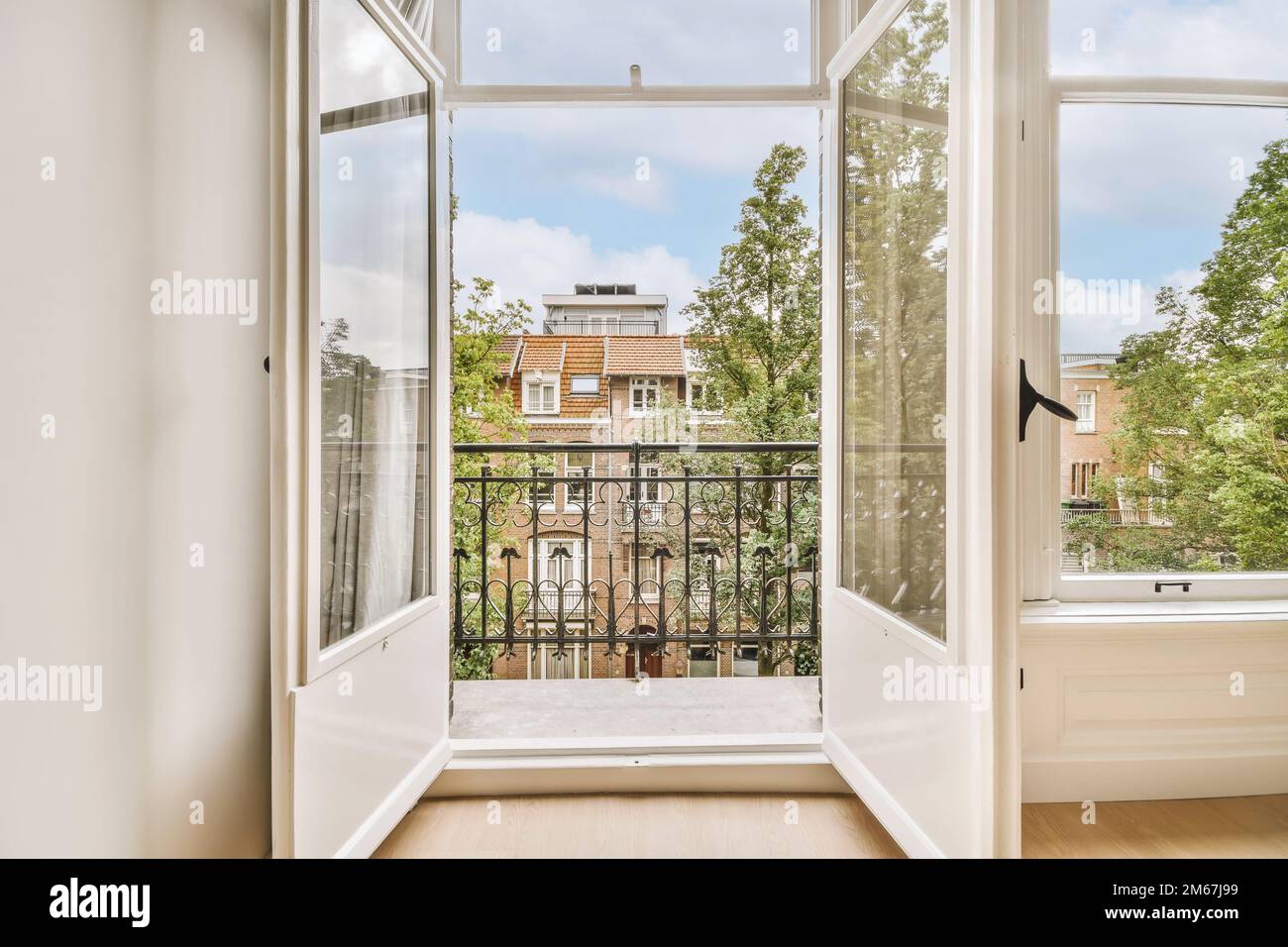 Ein offenes Fenster mit Blick auf die Straße von einem Zimmer mit Holzfußboden und weißen Wänden, auf dem eine schwarze Katze sitzt Stockfoto