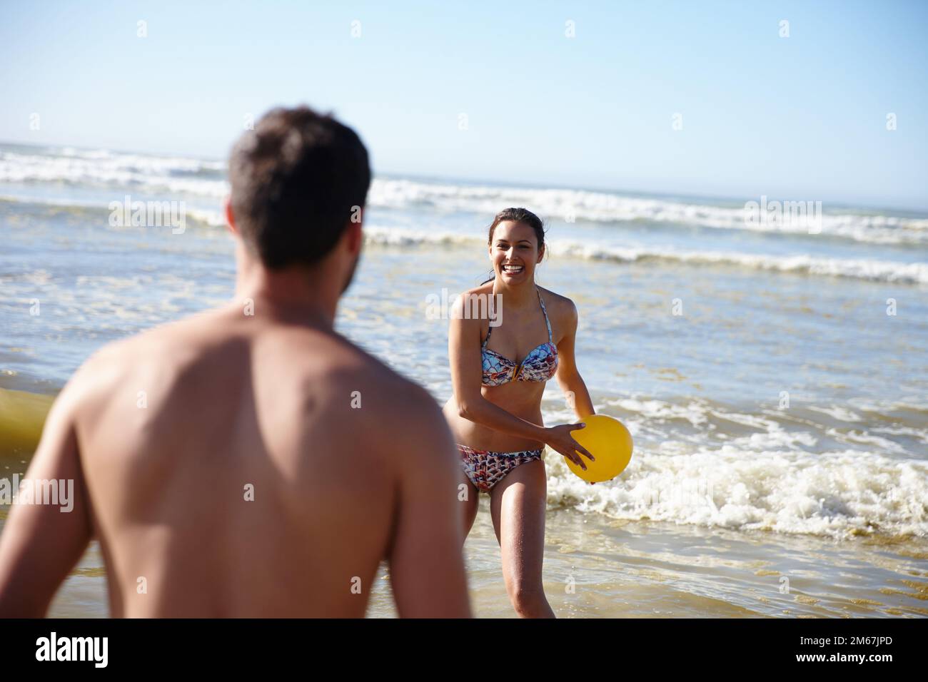 Bereit. Ein glückliches Paar, das im flachen Wasser am Strand mit einem Ball spielt. Stockfoto