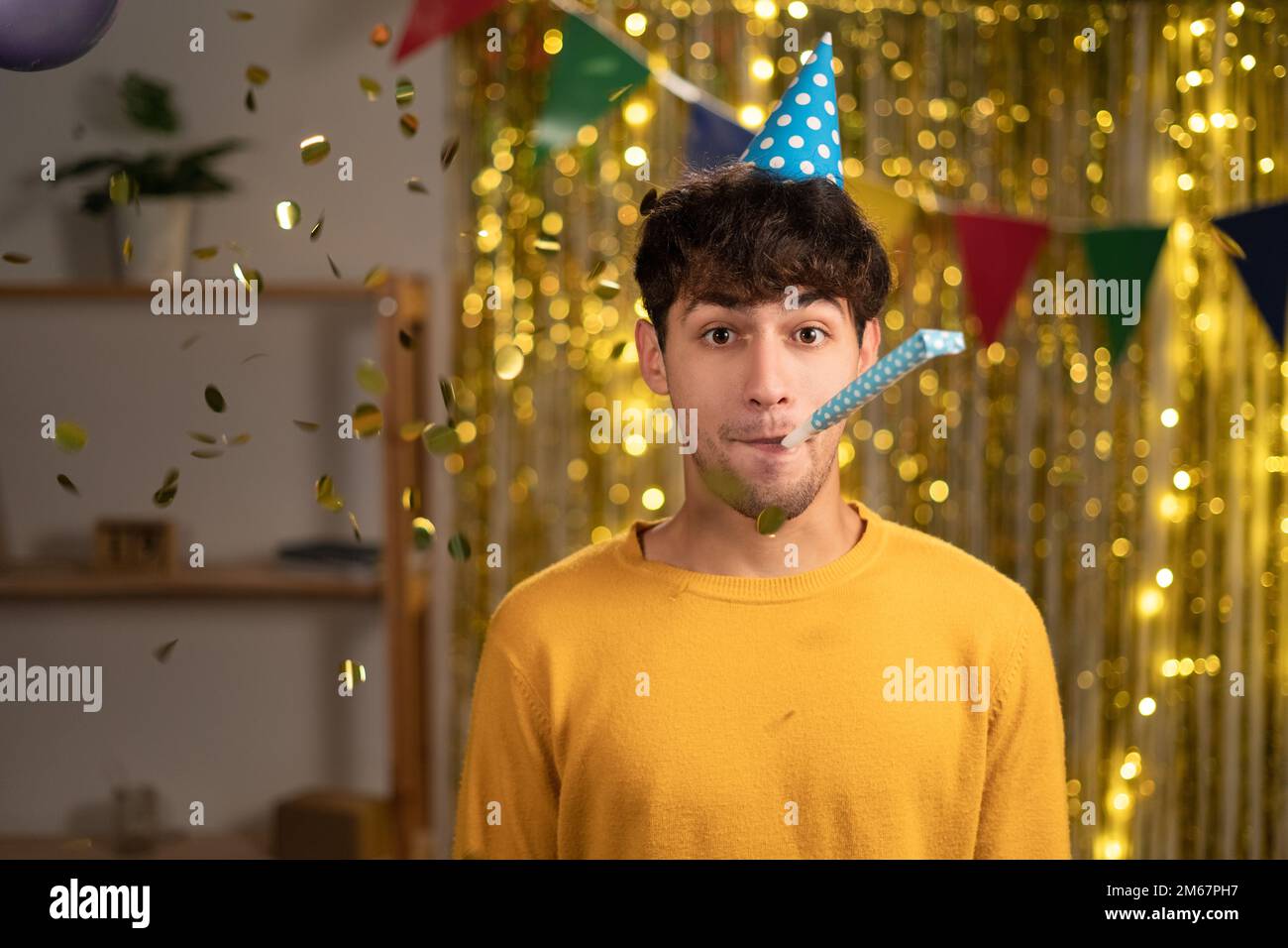 Ein hübscher junger arabischer Mann im Pullover bläst zu Hause Party Horn, feiert Geburtstag, hat selbstbewussten Ausdruck. Stockfoto