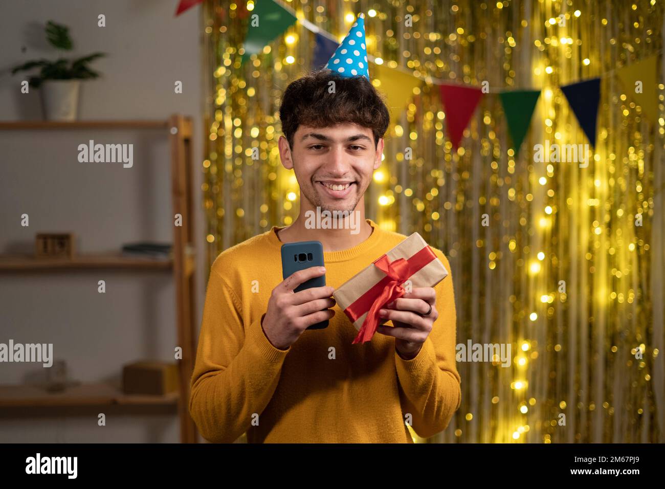 Ein glücklicher junger arabischer Mann erhielt online eine Geburtstagsgeschenkbestellung mit einer mobilen App Geburtstagsparty für Schüler Stockfoto