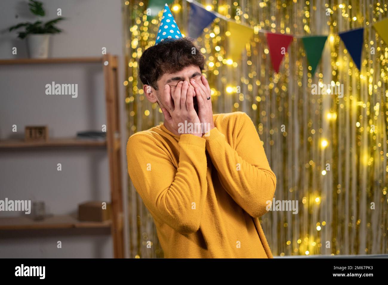 Aufgebracht, weinender junger Mann mit Partymütze, der seinen Geburtstag zu Hause feiert, unerwarteter Gast, Überraschung auf der Party Stockfoto