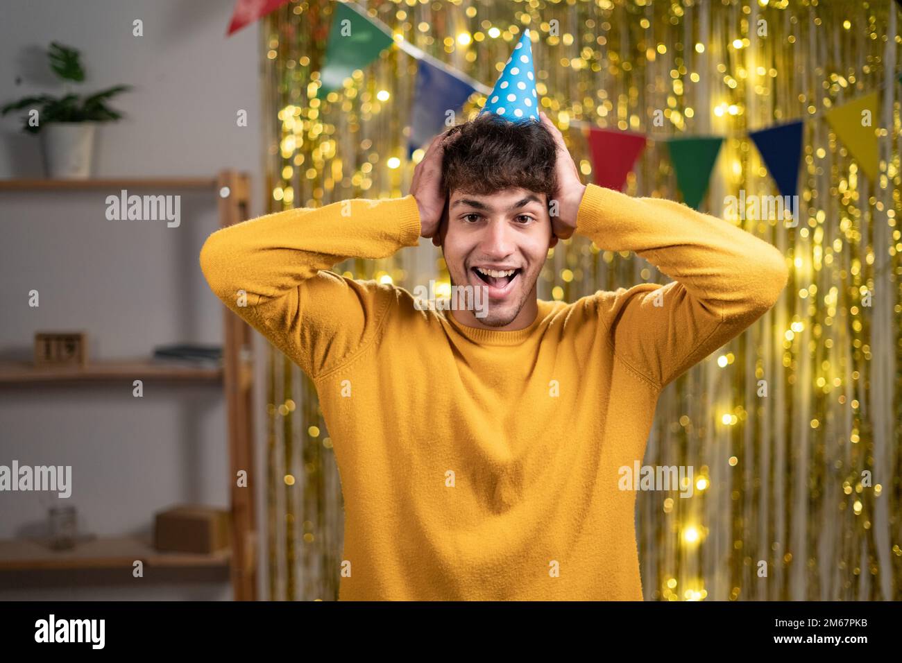Nahaufnahme Foto eines lustigen Mannes in festlicher Hasslaune zuhören positive Nachrichten offener Mund Arme am Kopf Kleidung Freizeit gelb warmer Pullover. Geburtstagsfeier zu Hause Stockfoto