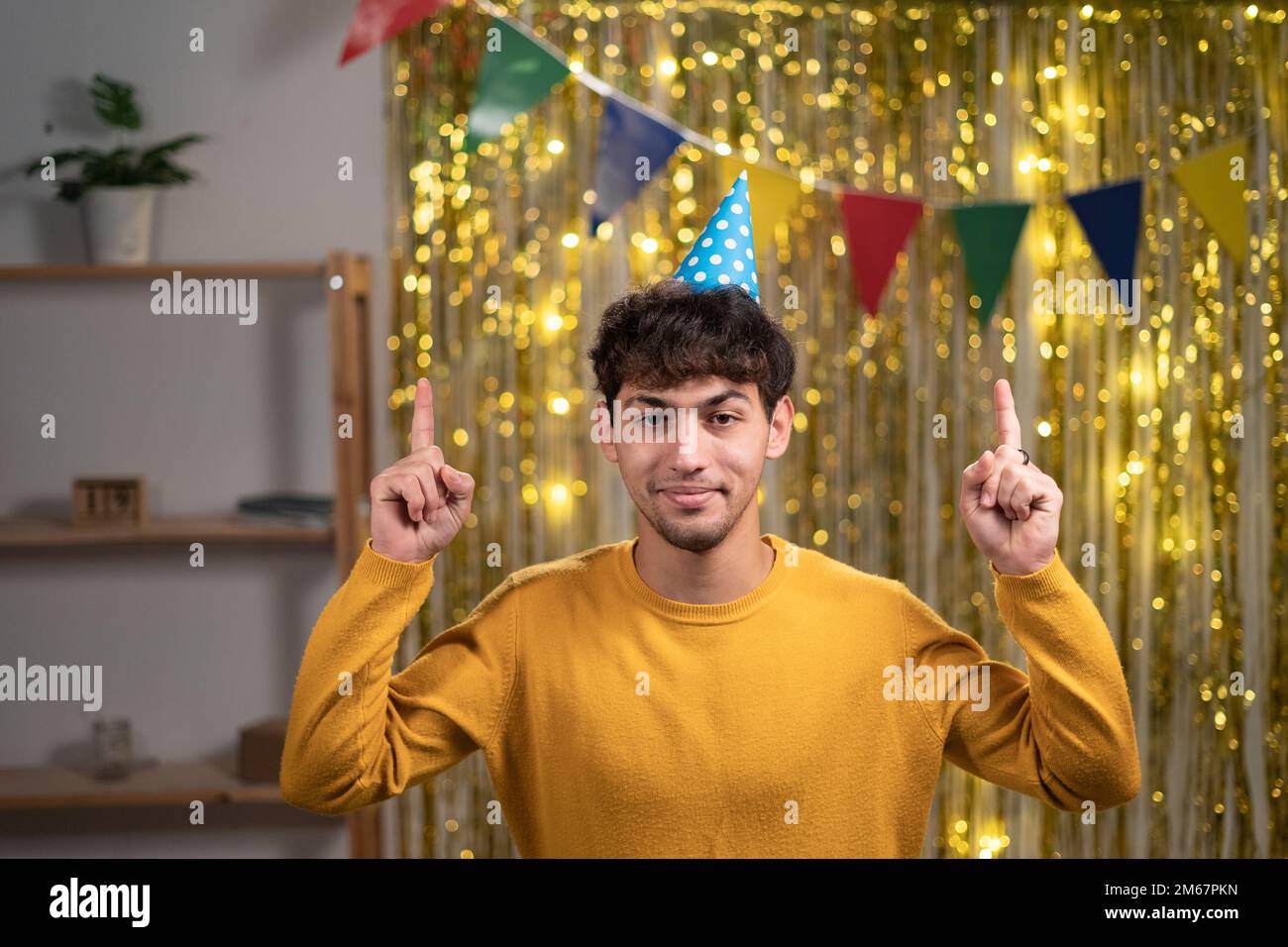 Ein Araber mit weihnachtlichem Hut, der Finger in den leeren Raum zeigt, Käufern niedrige Preise empfiehlt, und einen legeren gelben Pullover trägt, der seinen Geburtstag feiert Stockfoto
