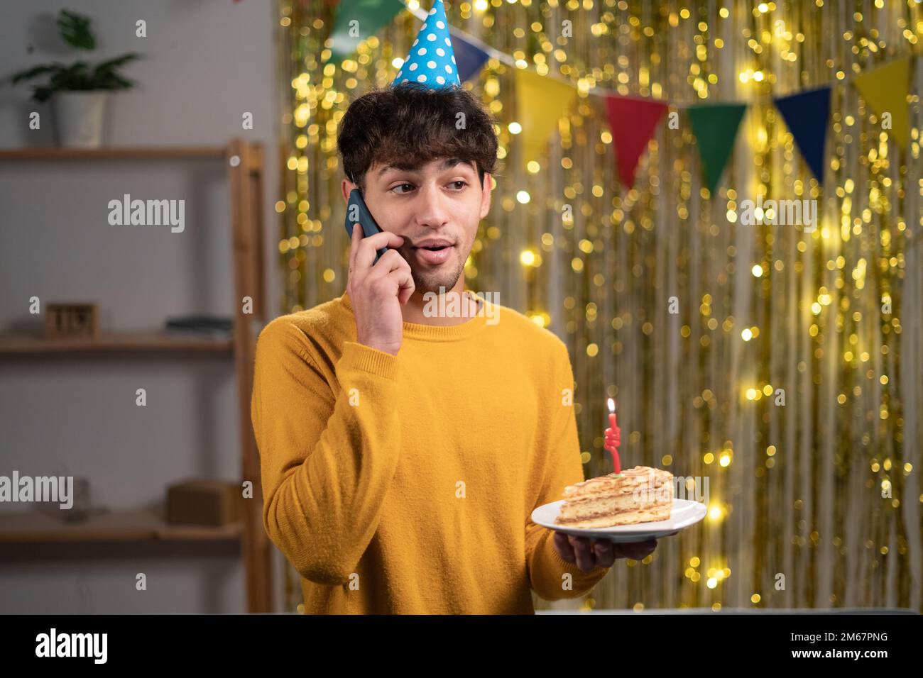 Ein junger araber feiert zu Hause Geburtstag und spricht am Handy und hält Geburtstagskuchen in den Händen Stockfoto