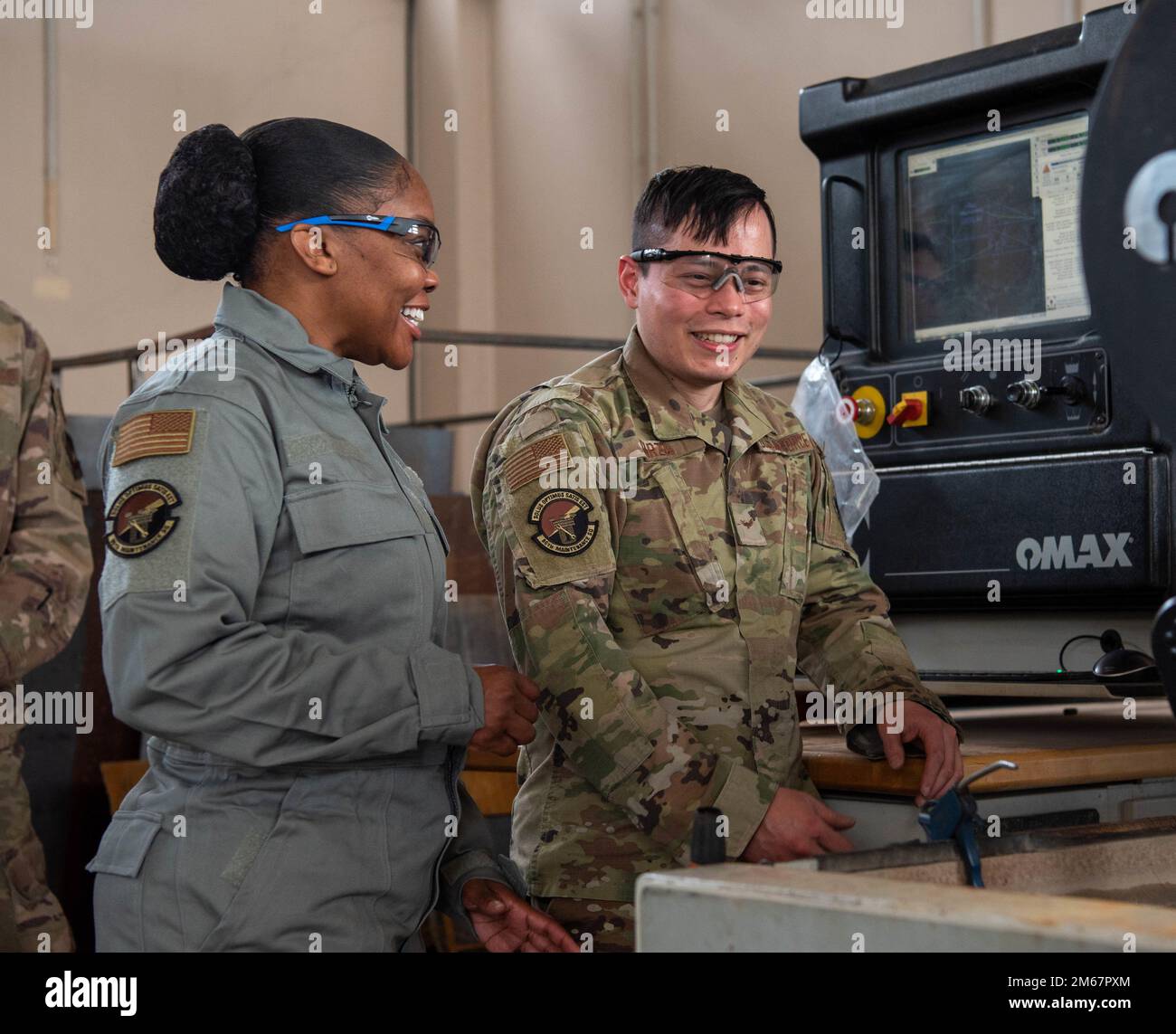 USA Air Force 86. Airlift Wing Kommandoleiter Master Sgt. Charmaine Kelley spricht mit Airman 1. Class Kevin Garza, 86. Maintenance Squadron Aircraft Metallic Technology Journeyman, am Luftwaffenstützpunkt Ramstein, Deutschland, 13. April 2022. Garza demonstrierte den Einsatz einer Wasserstrahlmaschine, die zum effizienten und genauen Ausschneiden von Teilen aus Plattenmaterialien verwendet wird, im Gegensatz zu manuellen Methoden mit Schleifmaschinen und Sägen. Stockfoto