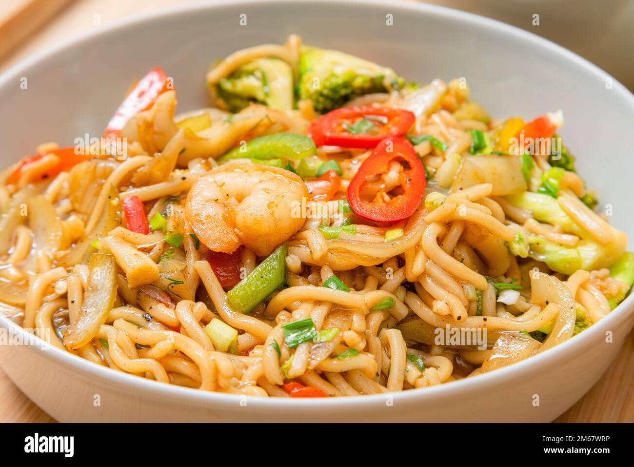 Goldfarbene würzige Meeresfrüchte-Nudeln mit Garnelen, Brokkoli, Chili in einem Teller auf einem Holztisch Stockfoto