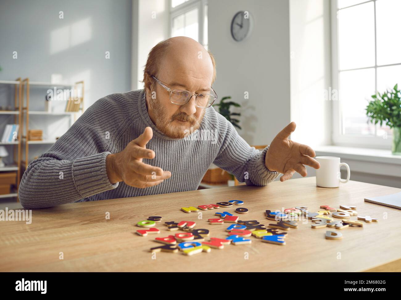 Alter Mann mit Alzheimer-Krankheit, der mit dem Alphabet am Tisch sitzt und Wörter erfindet Stockfoto