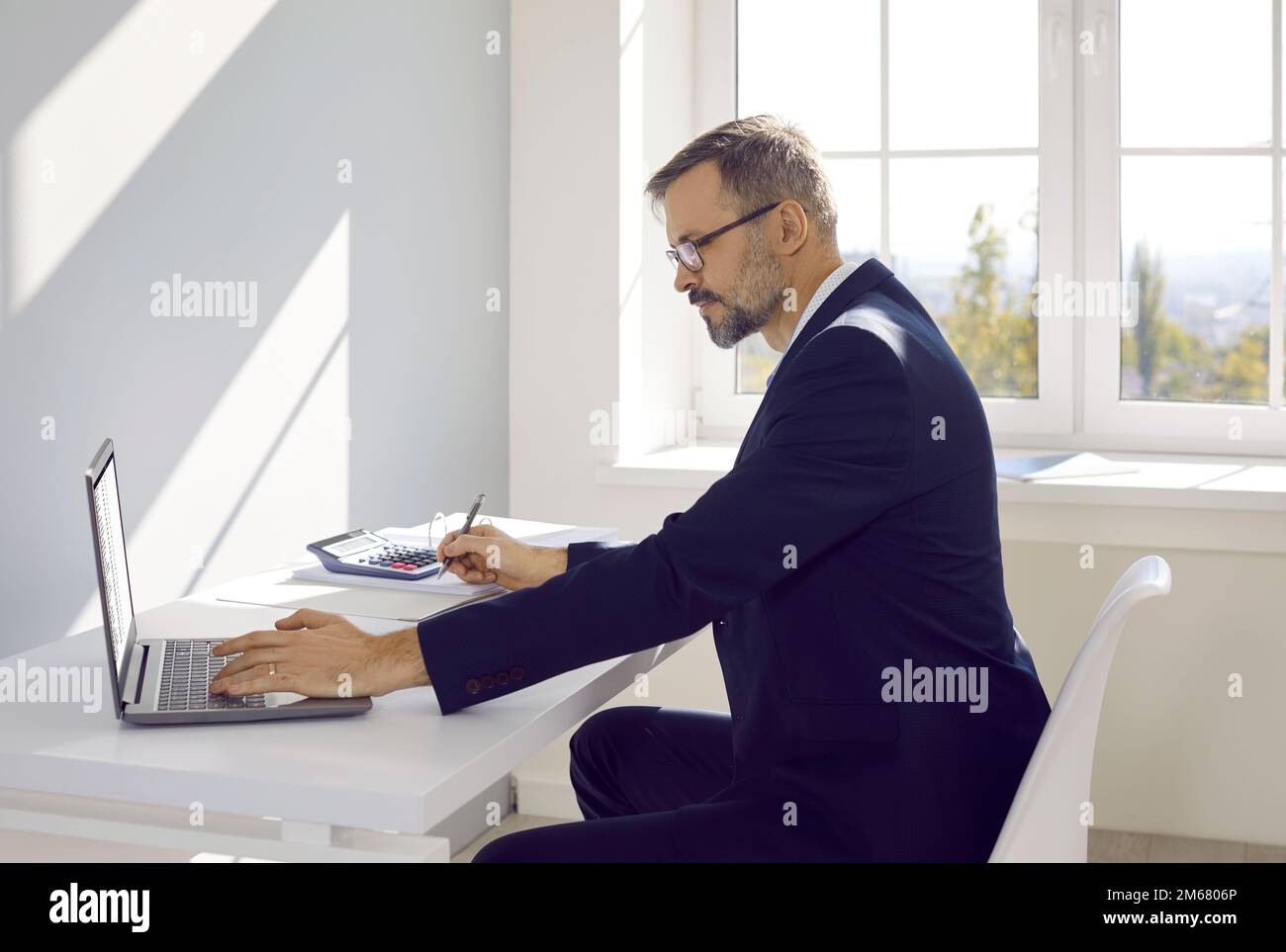 Erfahrener Buchhalter oder Prüfer, der mit einem Laptop im Büro arbeitet, sitzt am Tisch, Seitenansicht. Stockfoto