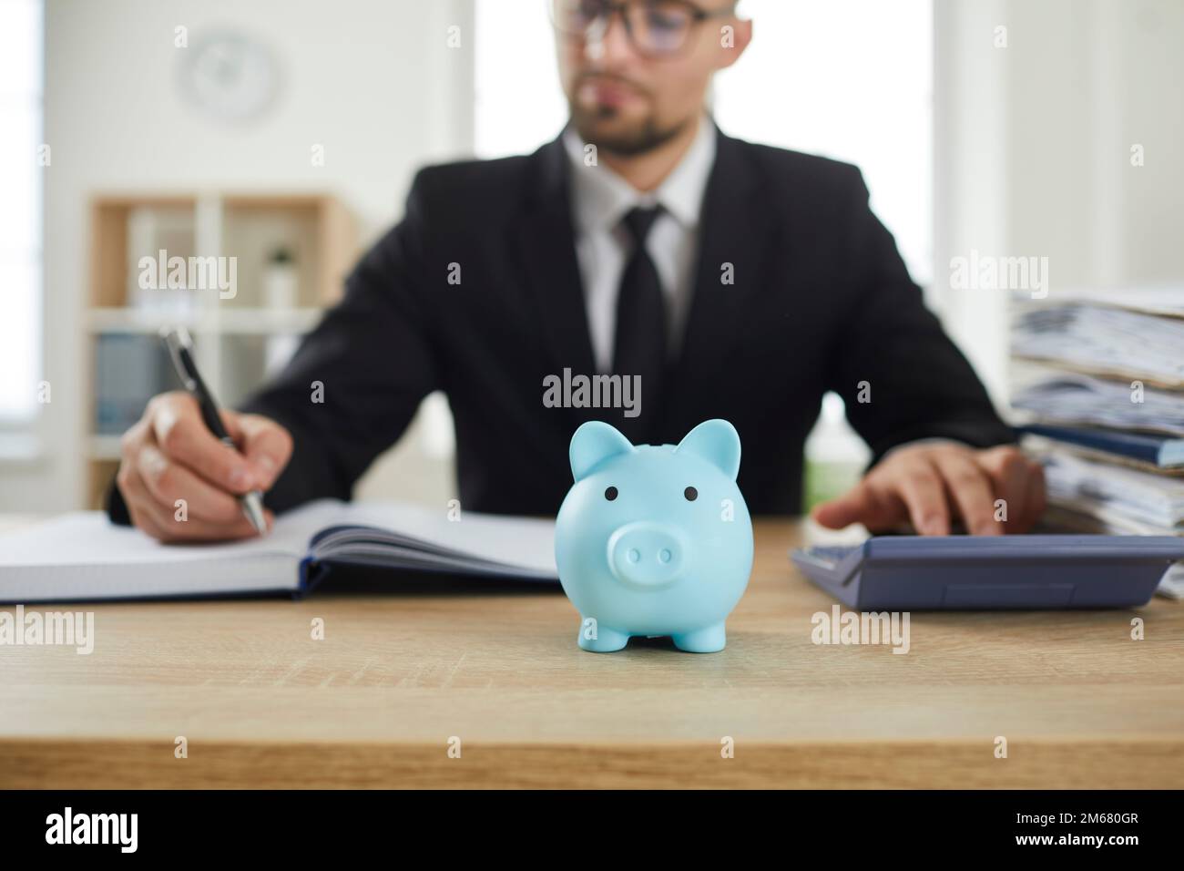 Sparschwein auf dem Schreibtisch eines Buchhalters, der mit einem Rechner das Budget analysiert und Berechnungen anstellt. Stockfoto