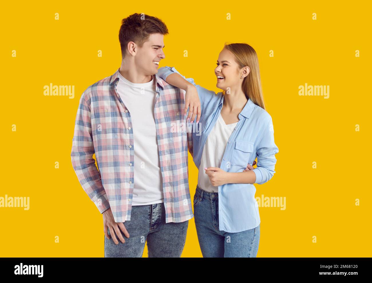 Ein fröhliches junges Paar, das lächelnd lächelt und sich isoliert auf gelbem Studiohintergrund ansieht. Stockfoto