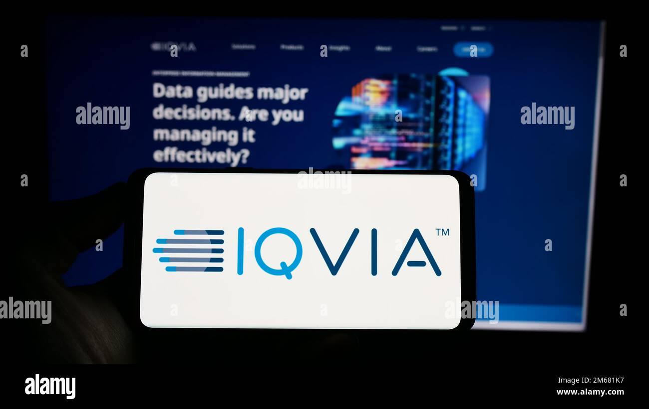 Person, die ein Mobiltelefon mit dem Logo des US-amerikanischen Gesundheitstechnologieunternehmens IQVIA Holdings Inc. Auf dem Bildschirm vor der Webseite hält. Konzentrieren Sie sich auf das Display des Telefons. Stockfoto