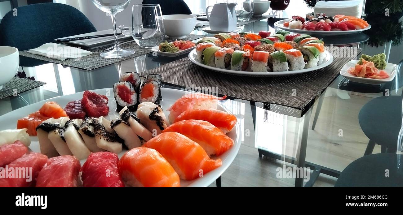 Gläserner Tisch zum Feiern. Japanisches Sushi. Maki, Nigiri und Sashimi mit Thunfisch, Lachs, Garnelen und Avocado Stockfoto